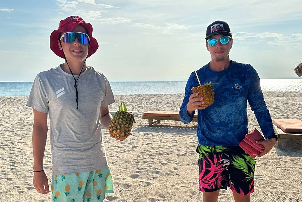 Two young guests enjoying tropical drinks on the sandy beach, showcasing the relaxed vibe of a Belize all-inclusive family resort.